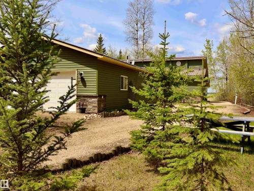 Green horizontal siding exterior with a white paneled garage door and stone-clad foundation - #26 5508 Twp Rd 593A, Rural Barrhead County, AB - Outdoor