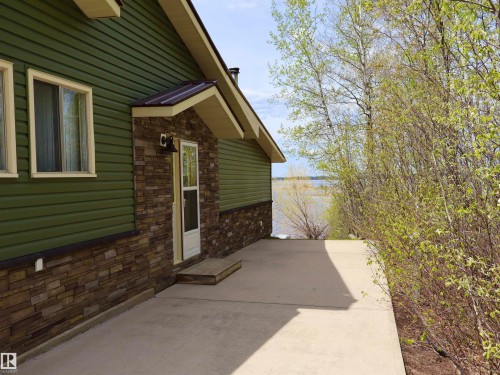 Exterior featuring green horizontal siding, stacked stone veneer, a covered entry, and a concrete patio - #26 5508 Twp Rd 593A, Rural Barrhead County, AB - Outdoor With Exterior