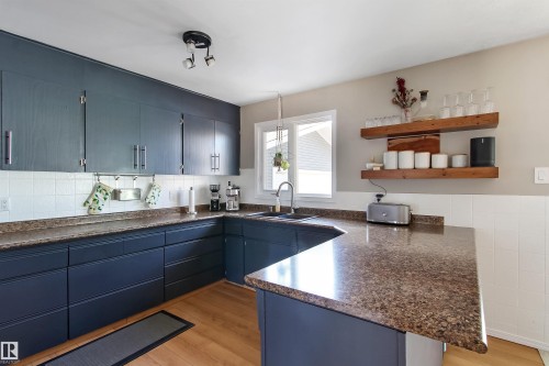 Kitchen featuring dark cabinetry, light-toned wood-finish flooring, and speckled countertops - 803 12 Avenue, Cold Lake, AB - Indoor Photo Showing Kitchen With Double Sink