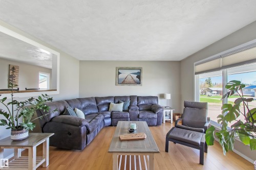 Bright living space featuring wood-finish flooring, a large picture window with roller shades, and a pass-through opening to an adjacent room - 803 12 Avenue, Cold Lake, AB - Indoor Photo Showing Living Room