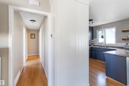Hallway with wood-finish flooring and a kitchen featuring dark cabinetry, a double window, and a peninsula with a stone-finish countertop - 803 12 Avenue, Cold Lake, AB - Indoor Photo Showing Kitchen