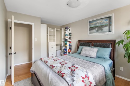 Bedroom featuring wood-finish flooring, built-in closet organization system with shelving and drawers, a white door with black hardware, and light neutral wall paint - 803 12 Avenue, Cold Lake, AB - Indoor Photo Showing Bedroom