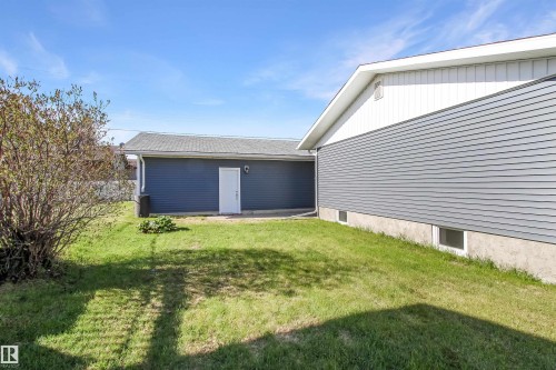 Expansive green lawn with a detached garage featuring blue siding and a white door - 803 12 Avenue, Cold Lake, AB - Outdoor With Exterior