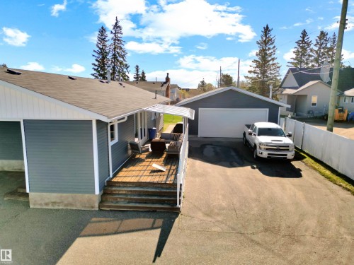 Rear exterior featuring a spacious wooden deck with steps, a detached garage with a white overhead door, a paved driveway, and blue horizontal siding - 803 12 Avenue, Cold Lake, AB - Outdoor