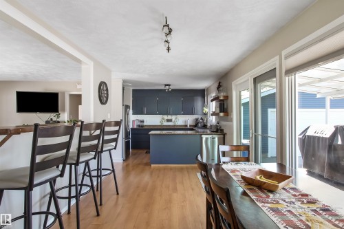 Open-concept kitchen and dining area featuring wood-finish flooring, custom dark blue cabinetry, and stainless steel appliances - 803 12 Avenue, Cold Lake, AB - Indoor Photo Showing Dining Room