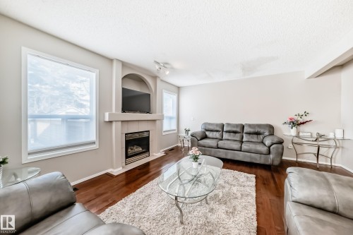 Living area featuring wood-finish flooring, a built-in fireplace with a mantel, an arched alcove, and multiple windows - 19024 50 Avenue, Edmonton, AB - Indoor Photo Showing Living Room With Fireplace