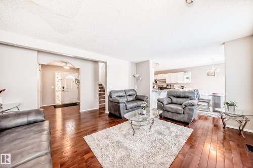 Spacious living area featuring wood-finish flooring, light neutral wall tones, and an arched entry to the front door - 19024 50 Avenue, Edmonton, AB - Indoor Photo Showing Living Room