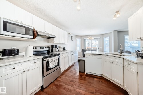 Kitchen featuring white cabinetry, light countertops, stainless steel appliances, and wood-finish flooring - 19024 50 Avenue, Edmonton, AB - Indoor Photo Showing Kitchen With Double Sink