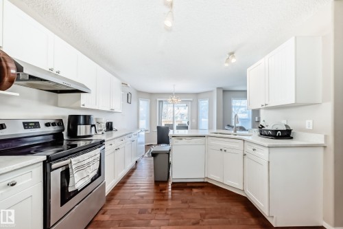 Kitchen featuring white cabinetry, light-toned countertops, stainless steel appliances, and wood-finish flooring - 19024 50 Avenue, Edmonton, AB - Indoor Photo Showing Kitchen