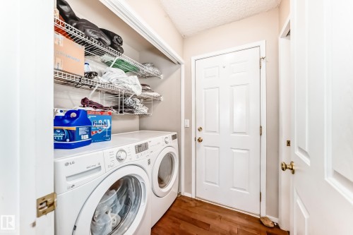 Dedicated laundry space featuring a white front-loading washer and dryer set, wire shelving, and wood-finish flooring - 19024 50 Avenue, Edmonton, AB - Indoor Photo Showing Laundry Room