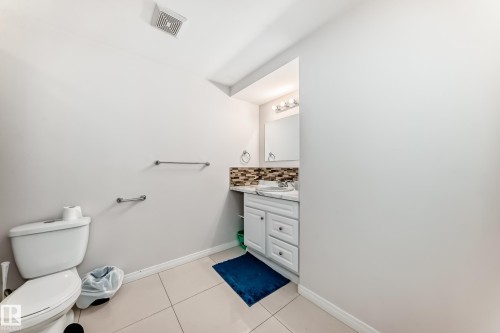 Bathroom featuring a white toilet, light-colored square floor tiles, a white vanity cabinet with a light-toned countertop, a rectangular mirror, and a mosaic tile backsplash - 19024 50 Avenue, Edmonton, AB - Indoor Photo Showing Bathroom