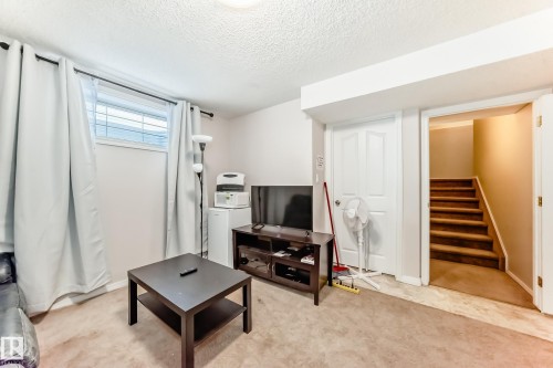 Carpeted living space featuring a window with blinds, a white door, and a staircase with carpeted treads - 19024 50 Avenue, Edmonton, AB - Indoor