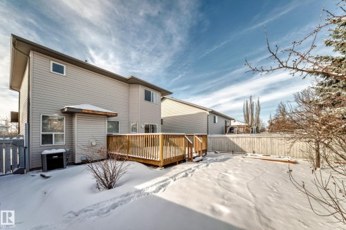 Rear exterior featuring light grey siding, multiple windows, a wooden deck with railing, and a fenced perimeter - 19024 50 Avenue, Edmonton, AB - Outdoor With Exterior