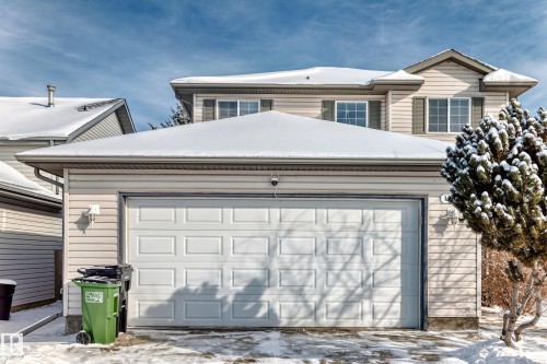 Two-story residential property featuring a double-wide garage door, beige horizontal siding, and multiple windows with dark shutters - 19024 50 Avenue, Edmonton, AB - Outdoor
