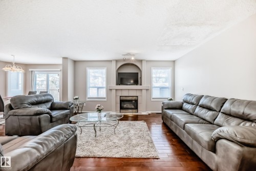 Spacious living area featuring wood-finish flooring, light-toned walls, and a prominent fireplace with an integrated media niche - 19024 50 Avenue, Edmonton, AB - Indoor Photo Showing Living Room With Fireplace