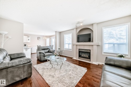 Living area featuring rich wood-finish flooring and a central fireplace with an arched media niche - 19024 50 Avenue, Edmonton, AB - Indoor Photo Showing Living Room With Fireplace