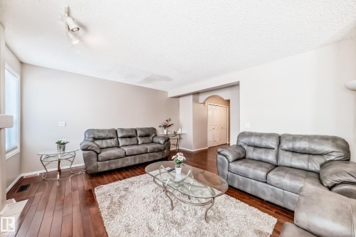 Spacious living area featuring wood-finish flooring, a neutral color palette, track lighting, a large window with blinds, and an arched doorway leading to bi-fold doors - 19024 50 Avenue, Edmonton, AB - Indoor Photo Showing Living Room