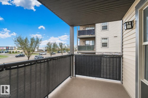 Outdoor balcony featuring a textured concrete floor, dark privacy screening, and an exterior wall light fixture - 206 103 Ambleside Drive, Edmonton, AB - Outdoor With Balcony With Exterior