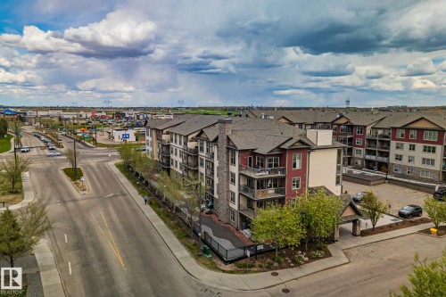 Multi-story residential building featuring a stone and siding exterior, private balconies, a covered entryway, and mature landscaping - 206 103 Ambleside Drive, Edmonton, AB - Outdoor With Balcony With View