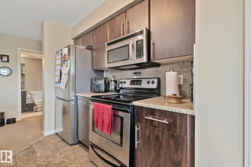 Kitchen featuring wood-finish cabinetry, stainless steel appliances, speckled countertops, and a gray tiled backsplash - 206 103 Ambleside Drive, Edmonton, AB - Indoor Photo Showing Kitchen