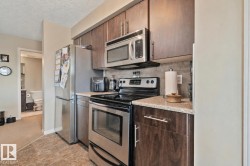 Kitchen featuring wood-finish cabinetry, stainless steel appliances, speckled countertops, and a gray tile backsplash - 