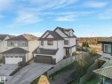 Modern two-story residence featuring a white exterior with dark trim accents, a two-car garage with a wood-finish door, a gabled roofline, and an enclosed backyard with a wooden fence - 6613 62 Avenue, Beaumont, AB  - Outdoor 