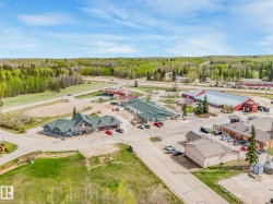 Aerial perspective showcasing a commercial development with multiple buildings, surrounding asphalt parking areas, and mature trees - 