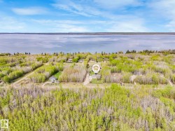 Expansive lakefront property featuring a broad body of water, dense tree cover, a clear blue sky, and a single-story residence - 