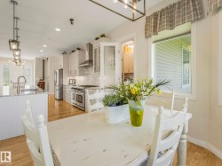 Open-concept kitchen and dining area featuring light wood-finish flooring, a kitchen island with a built-in sink, stainless steel appliances, and white cabinetry - 