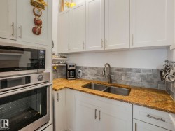Kitchen featuring white shaker-style cabinetry, a built-in stainless steel microwave and oven, a double basin stainless steel sink, and a gray subway tile backsplash - 