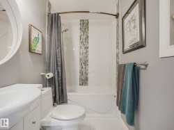 Bathroom featuring a built-in bathtub with a tile surround, mosaic tile accent, a white vanity with integrated sink, and a toilet - 