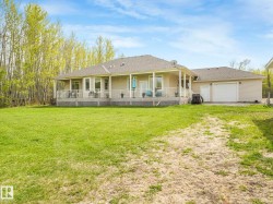 Expansive green lawn bordering a single-story home with a tan exterior, a covered rear porch, and an attached garage - 