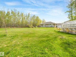 Expansive green lawn with a greenhouse, bordered by a dense stand of deciduous trees - 