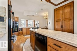 Kitchen featuring wood-finish cabinetry, light-toned stone countertops, integrated black appliances, a black basin sink with a gooseneck faucet, and a bay window - 