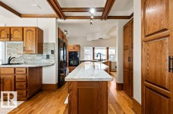 Kitchen featuring a central island with a light-toned countertop, wood-finish flooring, and exposed ceiling beams - 