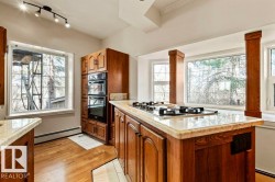 Kitchen featuring a built-in double oven, integrated gas cooktop, natural wood cabinetry, light-toned countertops, and multiple windows - 