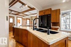 Kitchen island featuring a double basin sink with a matte black faucet, light-toned stone countertop, and wood-finish cabinetry - 