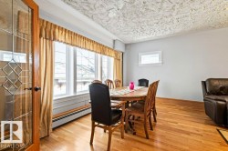 Light wood-finish flooring featuring a multi-pane window with a baseboard heater, a decorative glass-paneled door, light-toned walls, and a textured ceiling - 