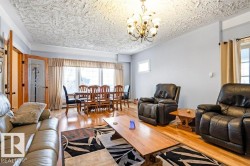 Hardwood flooring extends throughout this expansive living area, featuring a decorative ceiling texture and a multi-arm chandelier - 
