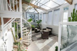 Bright sunroom featuring a white spiral staircase, extensive glass ceiling, and multiple large windows - 
