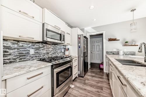 Modern kitchen featuring white cabinetry, stainless steel appliances, a mosaic tile backsplash, and light-toned countertops - 267 Sturtz Bend, Leduc, AB - Indoor Photo Showing Kitchen With Double Sink With Upgraded Kitchen