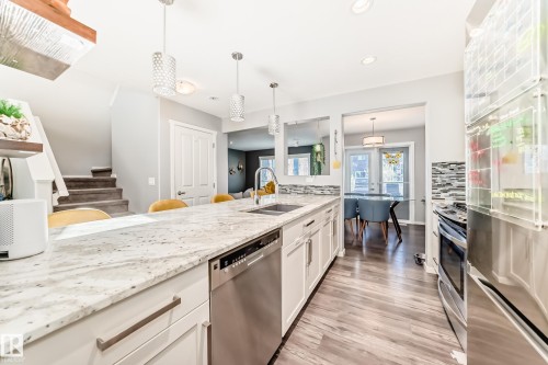 Kitchen island featuring a light-toned countertop, integrated stainless steel sink, and a built-in dishwasher - 267 Sturtz Bend, Leduc, AB - Indoor Photo Showing Kitchen With Double Sink With Upgraded Kitchen