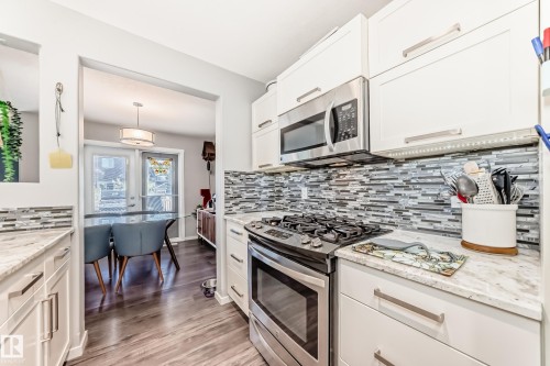 Kitchen featuring white cabinetry, light-toned countertops, a full-height mosaic tile backsplash, and stainless steel appliances, including an oven with a gas cooktop and an over-the-range microwave - 267 Sturtz Bend, Leduc, AB - Indoor Photo Showing Kitchen With Upgraded Kitchen
