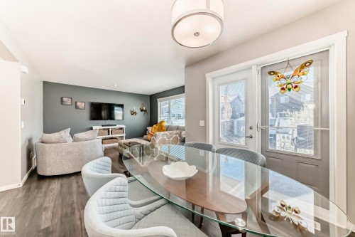 Open-concept dining and living area featuring wood-finish flooring, a contemporary glass-top dining table, and direct access to outdoor space via a glass panel door - 267 Sturtz Bend, Leduc, AB - Indoor Photo Showing Dining Room