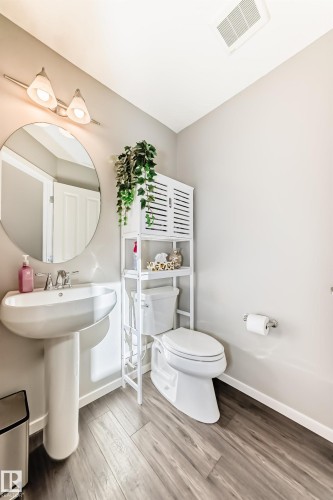 Pedestal sink with a circular mirror, wall-mounted light fixture, and wood-finish flooring - 267 Sturtz Bend, Leduc, AB - Indoor Photo Showing Bathroom
