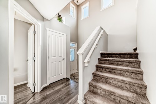 Two-story foyer featuring wood-finish flooring, a carpeted staircase with white railing, and multiple windows providing natural illumination - 267 Sturtz Bend, Leduc, AB - Indoor Photo Showing Other Room