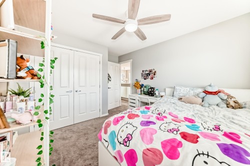 Carpeted bedroom featuring a ceiling fan with light fixture, built-in closet with bifold doors, and neutral wall paint - 267 Sturtz Bend, Leduc, AB - Indoor Photo Showing Bedroom
