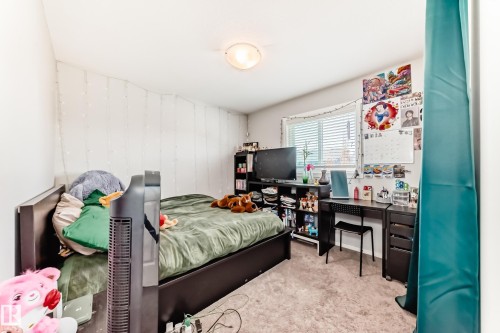Carpeted room featuring a single window with horizontal blinds, built-in shelving, a desk with drawers, and a ceiling-mounted light fixture - 267 Sturtz Bend, Leduc, AB - Indoor Photo Showing Bedroom
