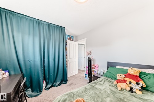 Spacious room featuring light gray walls, plush carpet flooring, a white paneled door, and a built-in closet area with teal curtains - 267 Sturtz Bend, Leduc, AB - Indoor Photo Showing Bedroom