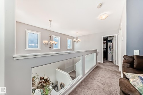 Upper-level hallway featuring a glass panel railing system, carpet flooring, multiple windows with white trim, and two hanging light fixtures - 267 Sturtz Bend, Leduc, AB - Indoor Photo Showing Other Room